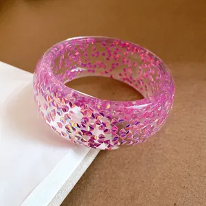 Primo piano di un bracciale rigido in resina trasparente con glitter viola iridescenti.