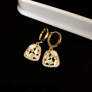 Close-up of 14k gold plated drop earrings with white cat's eye stones and sparkling zircons