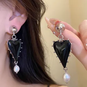 Detailed view of black resin heart earrings with baroque pearl drops and silver studs