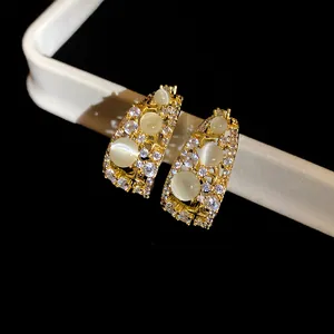 Detailed view of elegant C-shaped gold-plated earrings with cat eye stones and zircons