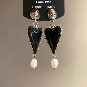 Detailed view of elegant black resin heart earrings featuring white pearls on a black display card