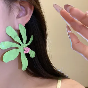 Detailed close-up of vibrant green floral drip oil earrings with pink center on ear