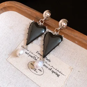 Detail shot of black resin heart earrings with elegant pearl drops on a vintage display card
