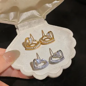 Detail of gold and silver heart-shaped zircon earrings in a cream seashell box