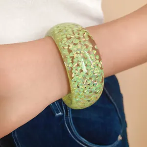 Primo piano di un bracciale a cerchio in resina verde chiaro iridescente con glitter.