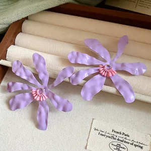 Macro detail of wavy purple flower earrings featuring pink beaded centers in a tray