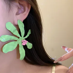 Detail view of oversized green pleated flower drop earrings worn by a female model