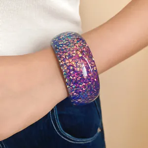Primo piano di un braccialetto rigido in resina colorata e iridescente indossato da donna.