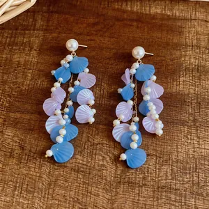 Detail of elegant shell sequin tassel earrings with pearls on wood background.