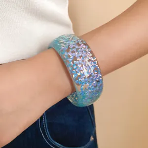 Dettaglio di un bracciale rigido in resina blu iridescente con glitter olografici