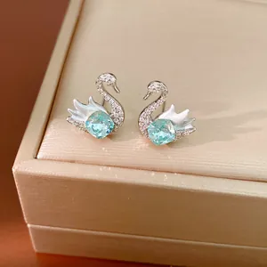 Detailed macro shot of silver swan stud earrings featuring a light blue cushion-cut crystal