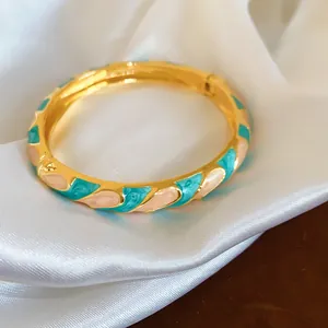 Vue détaillée d'un jonc doré élégant avec des motifs de pétales en émail bleu et pêche