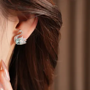 Close-up view of a sparkling swan stud earring with a light blue crystal on ear