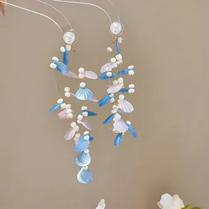 Macro detail of elegant long fairy-style earrings featuring blue leaf sequins and white pearls