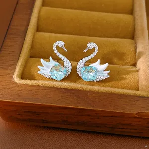 Close-up of swan stud earrings with blue square-cut zircons in a wooden jewelry box.