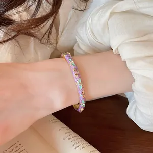 Gros plan d'un bracelet jonc en émail violet avec des fleurs dorées élégantes.