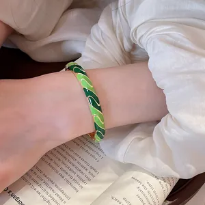 Gros plan d'un bracelet jonc en émail vert au poignet avec détails dorés élégants
