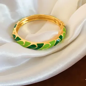 Gros plan d'un bracelet doré avec motifs floraux en émail vert sur soie blanche.