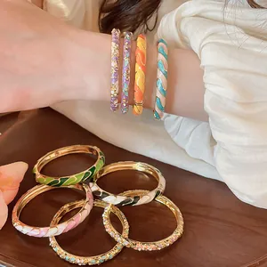 Gros plan de bracelets joncs en émail doré coloré avec motifs floraux et spirales.