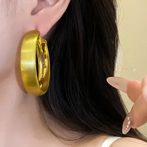 Detailed close-up of brushed gold hoop earrings with minimalist silver needle design