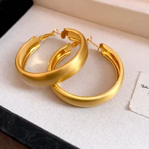 Close-up macro view of matte brushed golden hoop earrings showing fine metal texture