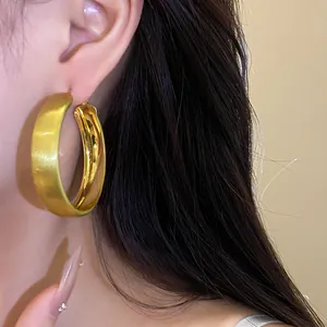 Detailed close-up of large brushed gold hoop earrings with matte and shiny finish