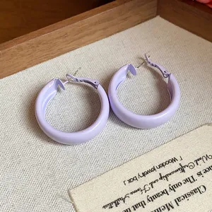 Close-up of lavender spray-painted hoop earrings on textured beige background