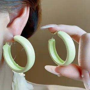 Detailed macro view of pale green lacquered minimalist hoop earrings shown on model