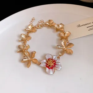 Dettaglio del braccialetto a fiori dorati con ciondolo floreale in smalto rosso