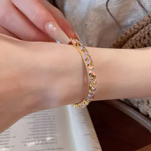 Vue détaillée d'un bracelet doré avec des fleurs en émail et des strass sur un poignet.