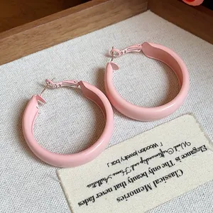 Close-up of minimalist pastel pink spray-painted hoop earrings on a textured background