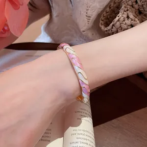 Gros plan sur un élégant jonc émaillé rose et blanc plaqué or porté au poignet