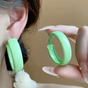 Close-up detail of vibrant green painted hoop earrings with glossy finish on ear