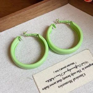 Detailed view of minimalist light green lacquered hoop earrings on textured fabric