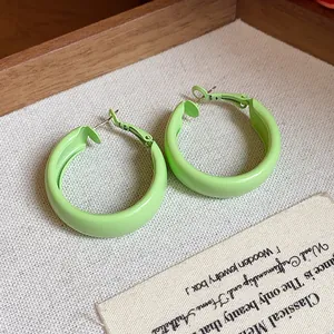 Close-up detail of light green spray-painted hoop earrings on a fine linen texture.