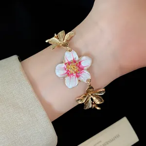 Dettaglio elegante di un bracciale vintage dorato con ciondoli a fiore in smalto sul polso.