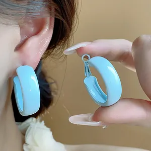Detailed close-up showing light blue enamel hoop earrings worn on ear and held by hand