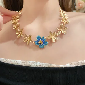 Primo piano di una collana girocollo a fiori dorati vintage con fiore in smalto blu centrale.