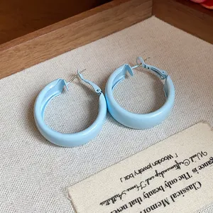 Macro view of dopamine light blue spray-painted hoop earrings inside a wooden jewelry tray