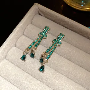 Close-up of silver teardrop earrings with emerald green crystals in a gray jewelry box