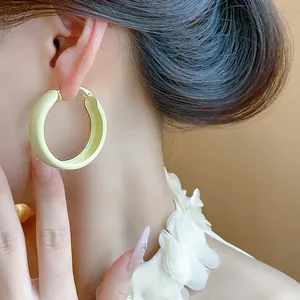 Close-up of a model wearing minimalist cream yellow spray-painted hoop earrings.
