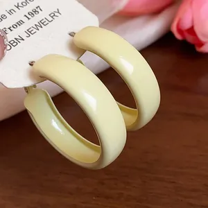 Detailed close-up showing glossy pale yellow spray-painted minimalist hoop earrings