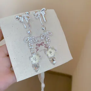 Detailed view of silver bow earrings with pearls and crystal drops on linen card