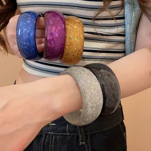 Macro view of colorful resin bangles with star sequins worn on wrist and held in hand.