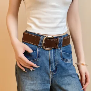 Detail of a brown leather belt with silver buckle and white stitching on denim jeans.