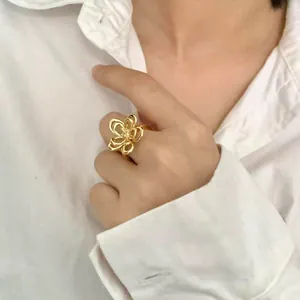 Close-up detail of an elegant gold minimalist hollow flower ring on a model's finger