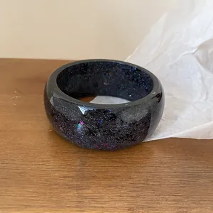 Close-up view of a thick black resin bangle featuring colorful iridescent glitter flakes