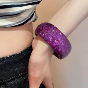 Close-up detail of a stylish purple resin bangle with sparkling glitter worn on a wrist.