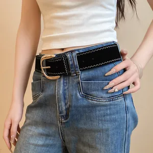 Close-up of black leather belt with white zigzag stitching and golden buckle on jeans