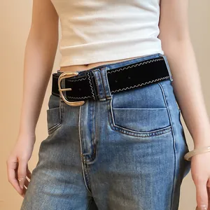 Close-up of black leather belt with gold horseshoe buckle and white zigzag stitching.